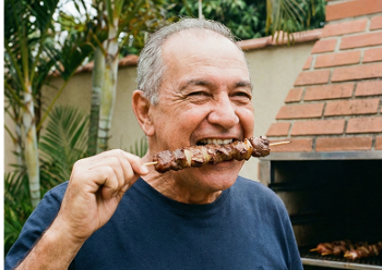 imagem de um senhor segurando um espeto de churrasco e sorrindo